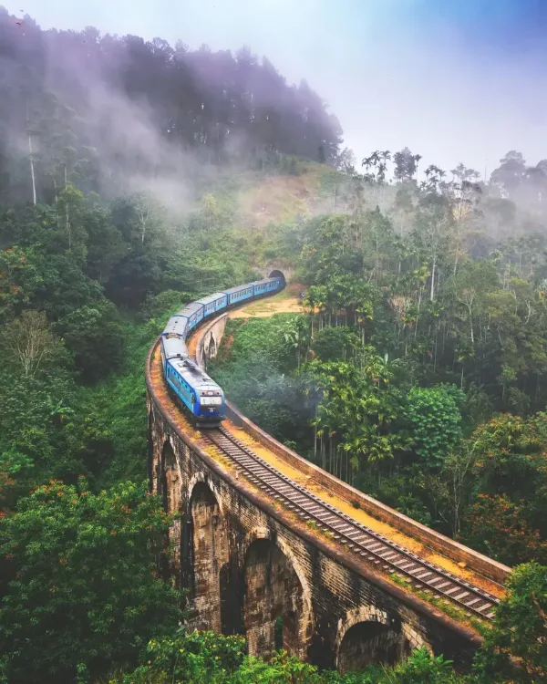 A train crossing the Nine Arches Bridge through misted hill country near Ella